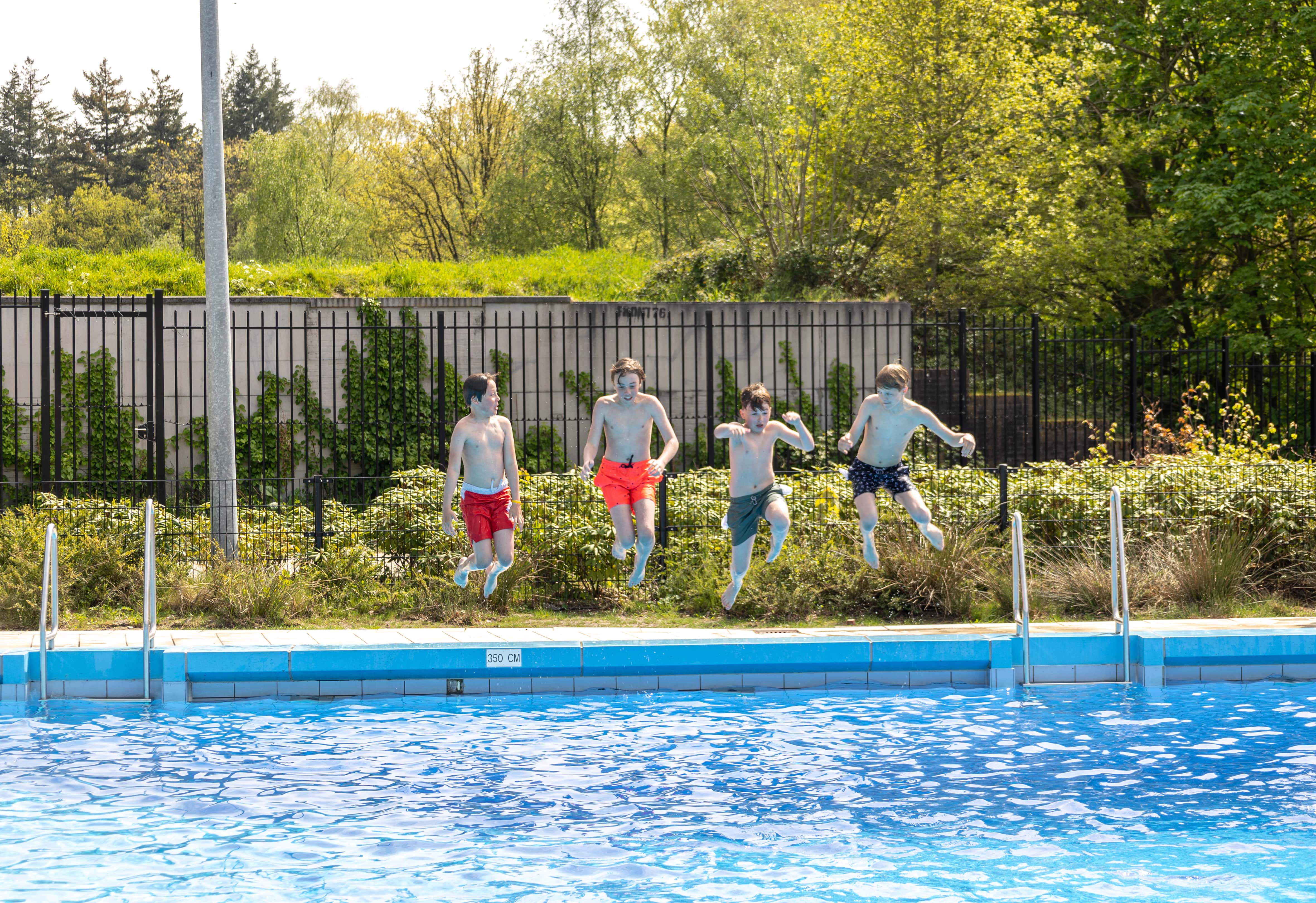 Vier jongens springen vol enthousiasme gelijktijdig in het buitenbad van Optisport.