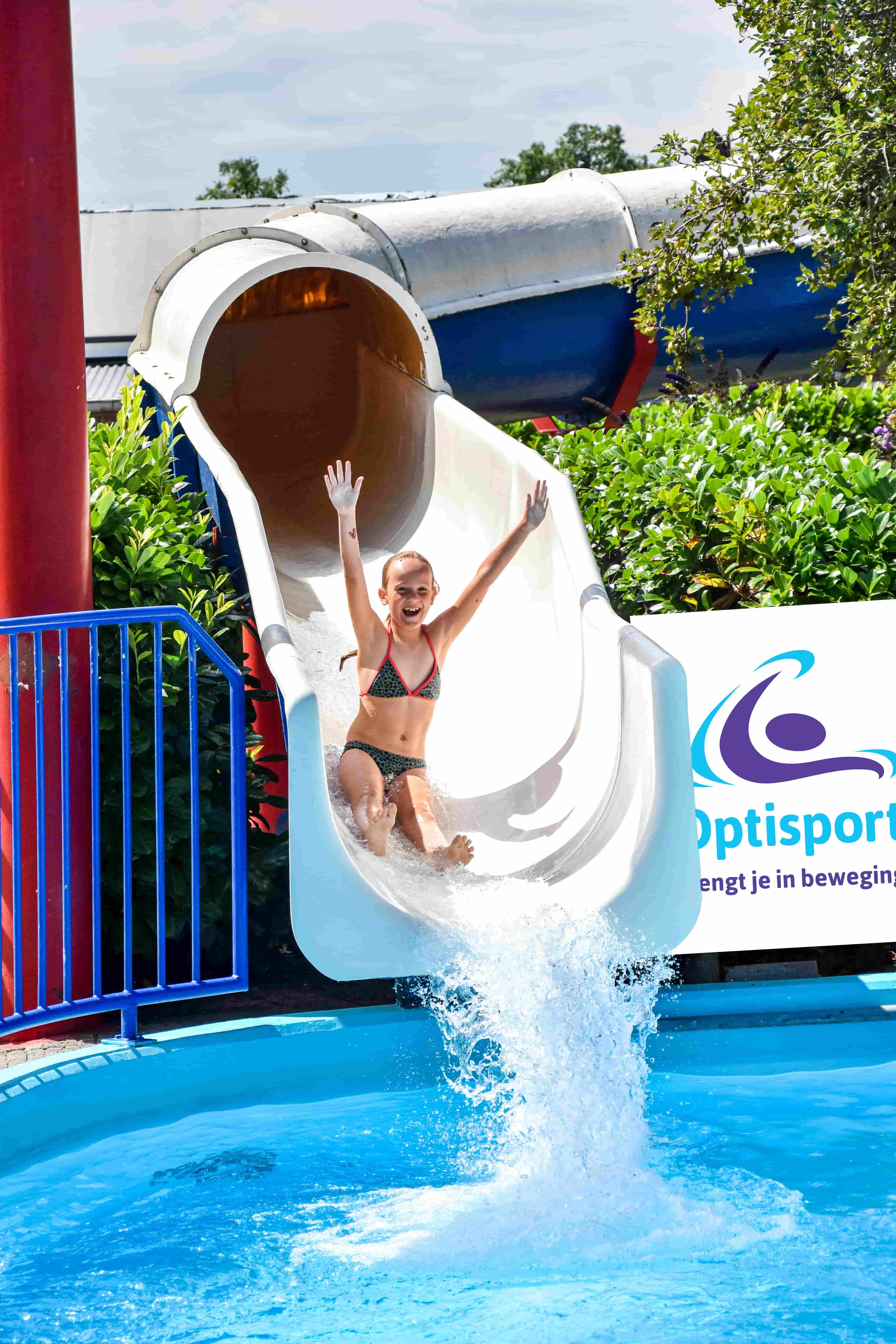 Met haar armen omhoog en juichend van de pret glijdt een meisje van de glijbaan af in een van de buitenbaden van Optisport.