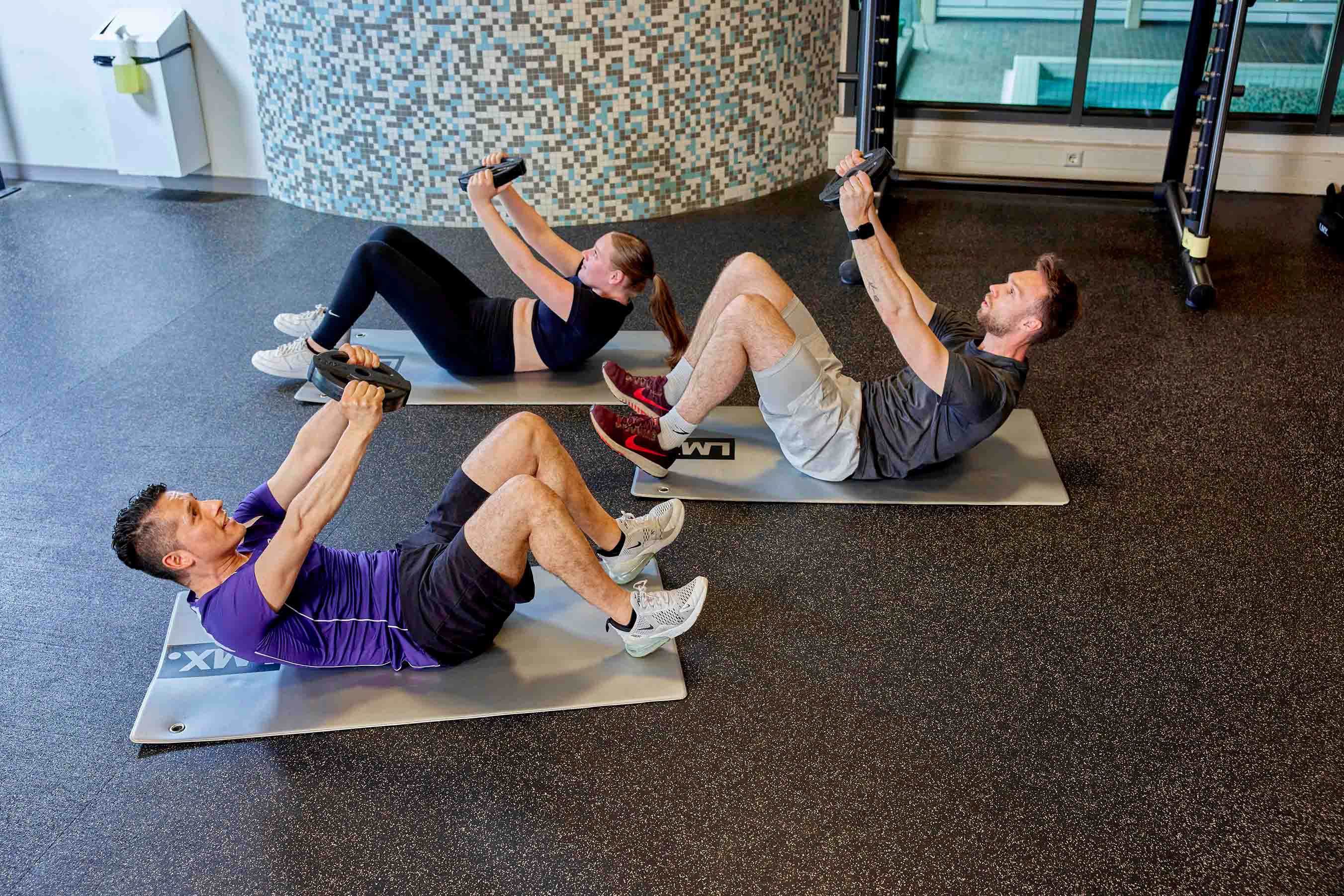 Drie sporters trainen op een matje tijdens de workout Club Core bij Optisport: in een half uur en met hoge intensiteit worden alle spiergroepen getraind. 
