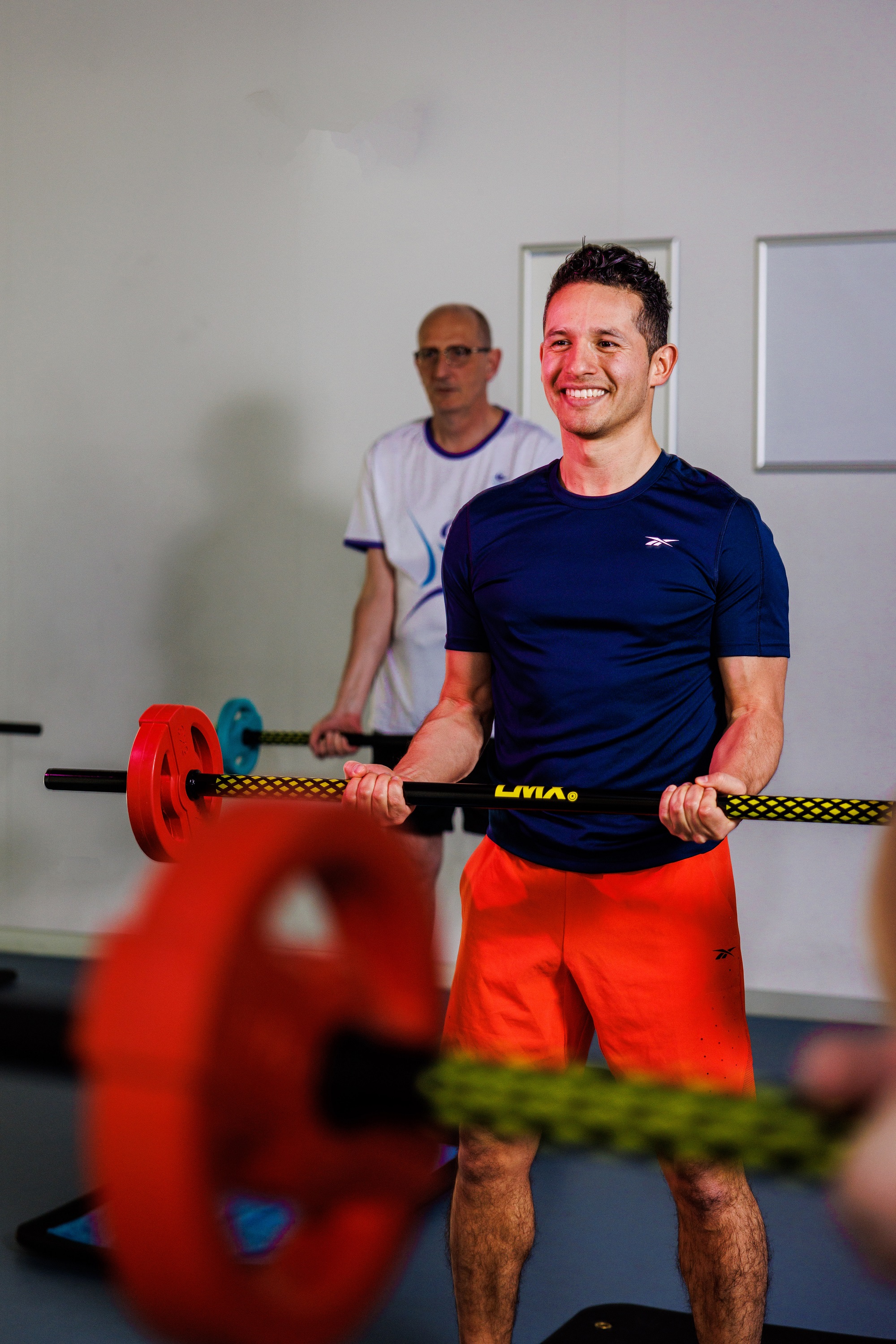 Tijdens een energieke les Club Power bij Optisport tillen sporters de barbell omhoog vanuit hun nek terwijl ze squats doen. 