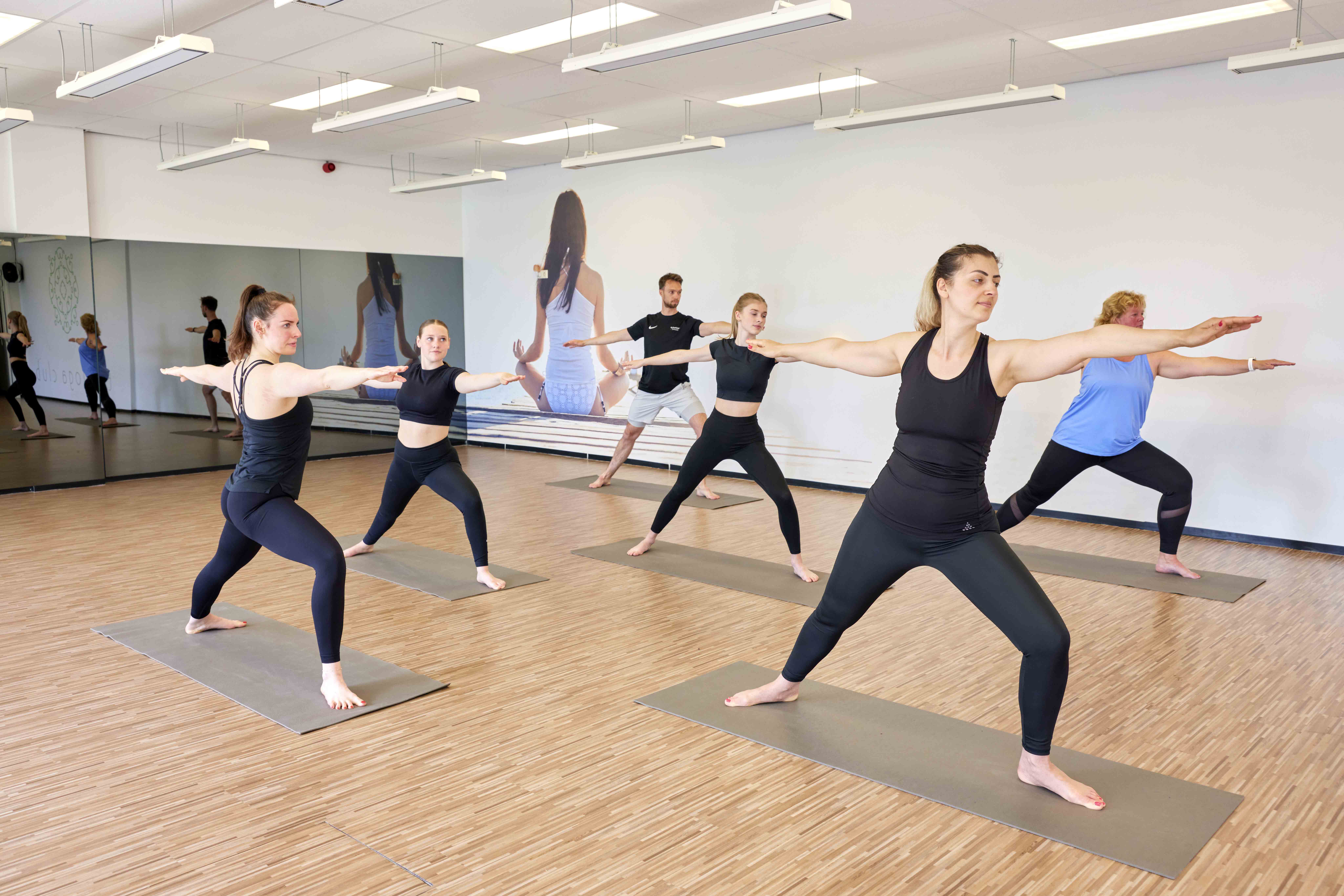 Een groep sporters doet yoga oefeningen tijdens een groepsles Club Yoga bij Optisport, om zo lichaam en geest in balans te houden. 