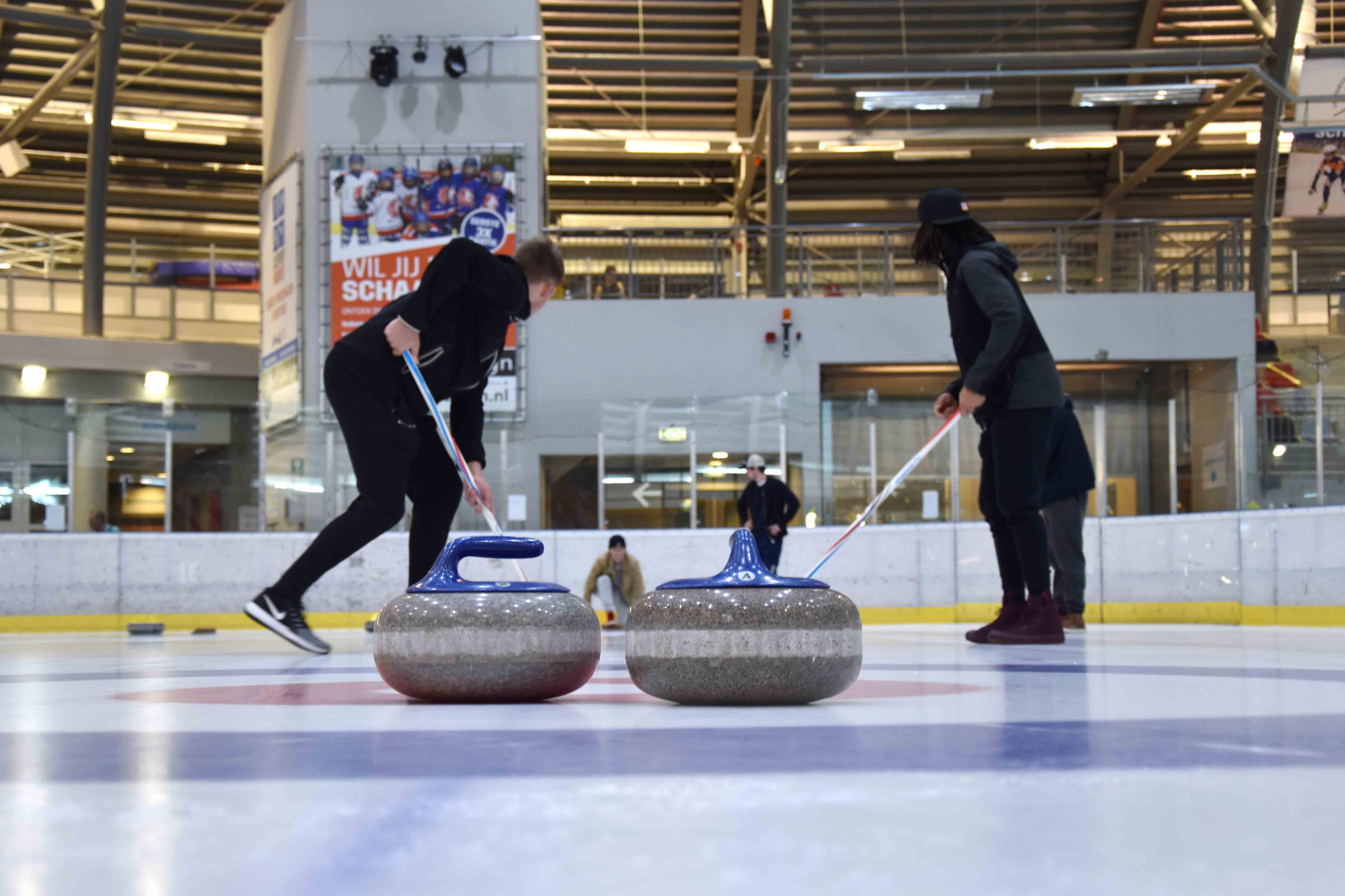 Vier mensen zijn bezig met een spel curling nadat ze een ijsbaan hebben gehuurd bij Optisport.