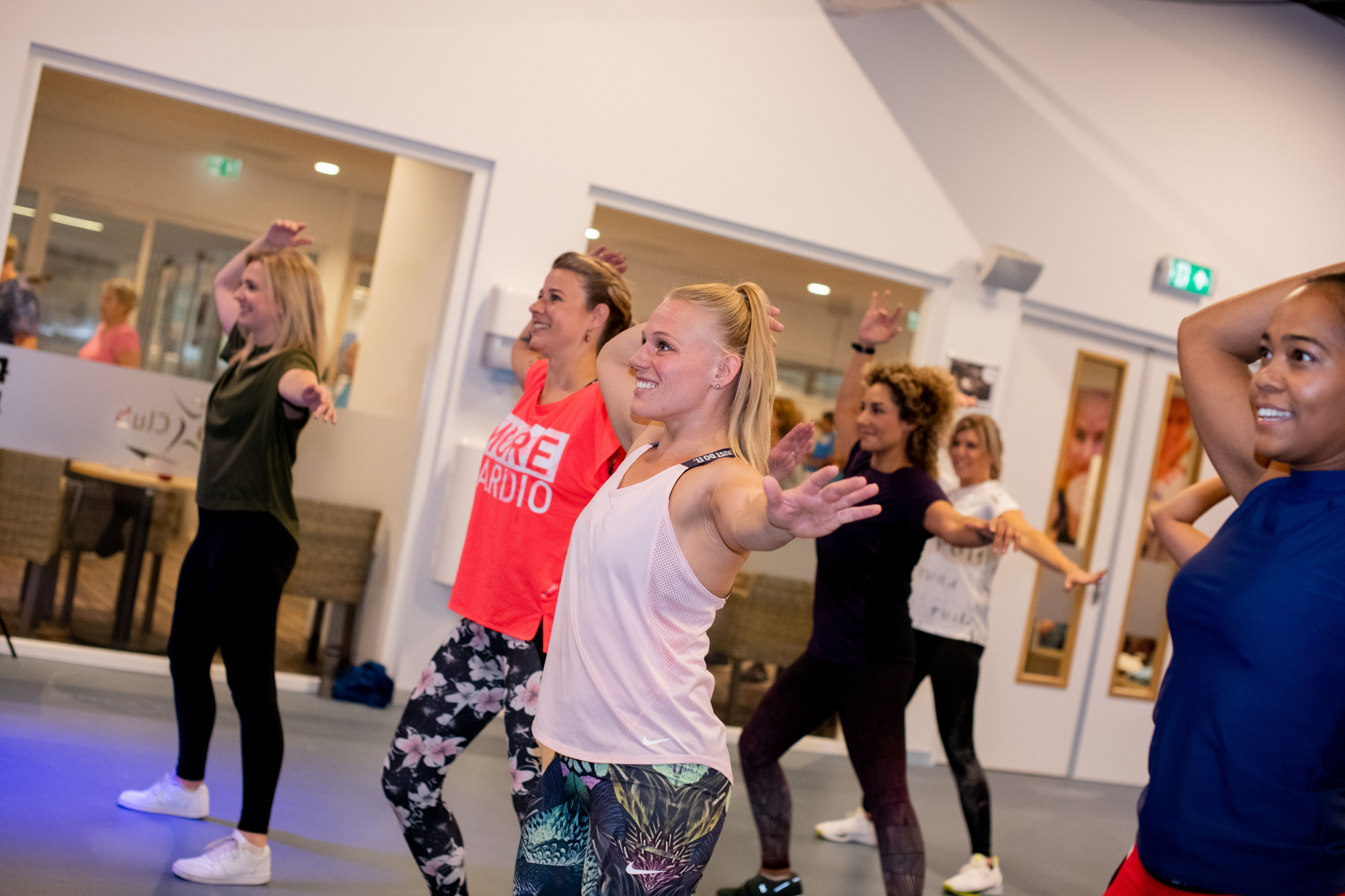 Een groep is bij Optisport aan het dansen tijdens een groepsles om fit te blijven. Onder begeleiding van een instructeur doen ze oefeningen.