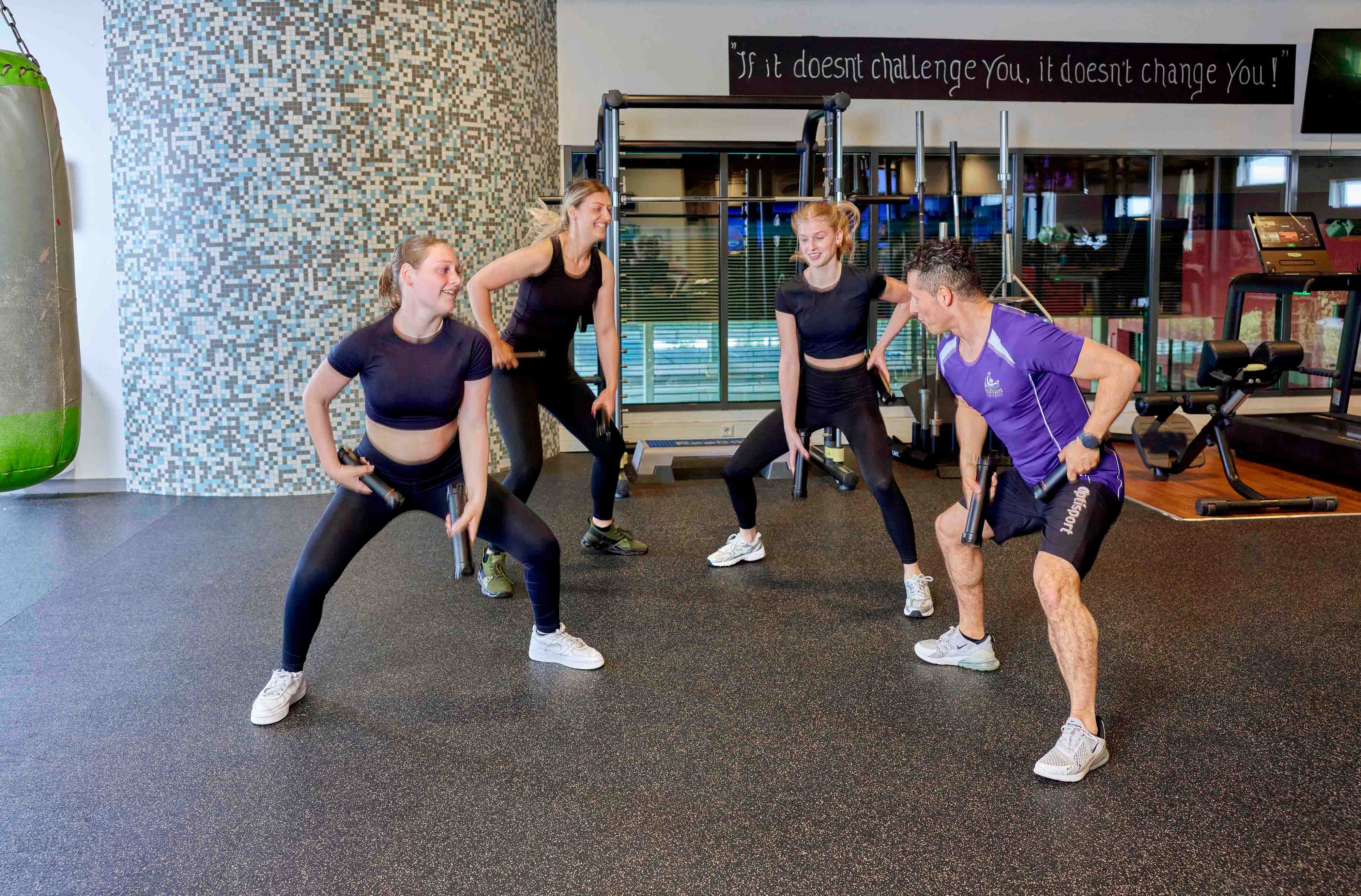 Een sportende vrouw staat op de crosstrainer en maakt een praatje met de ervaren instructeur van Optisport.