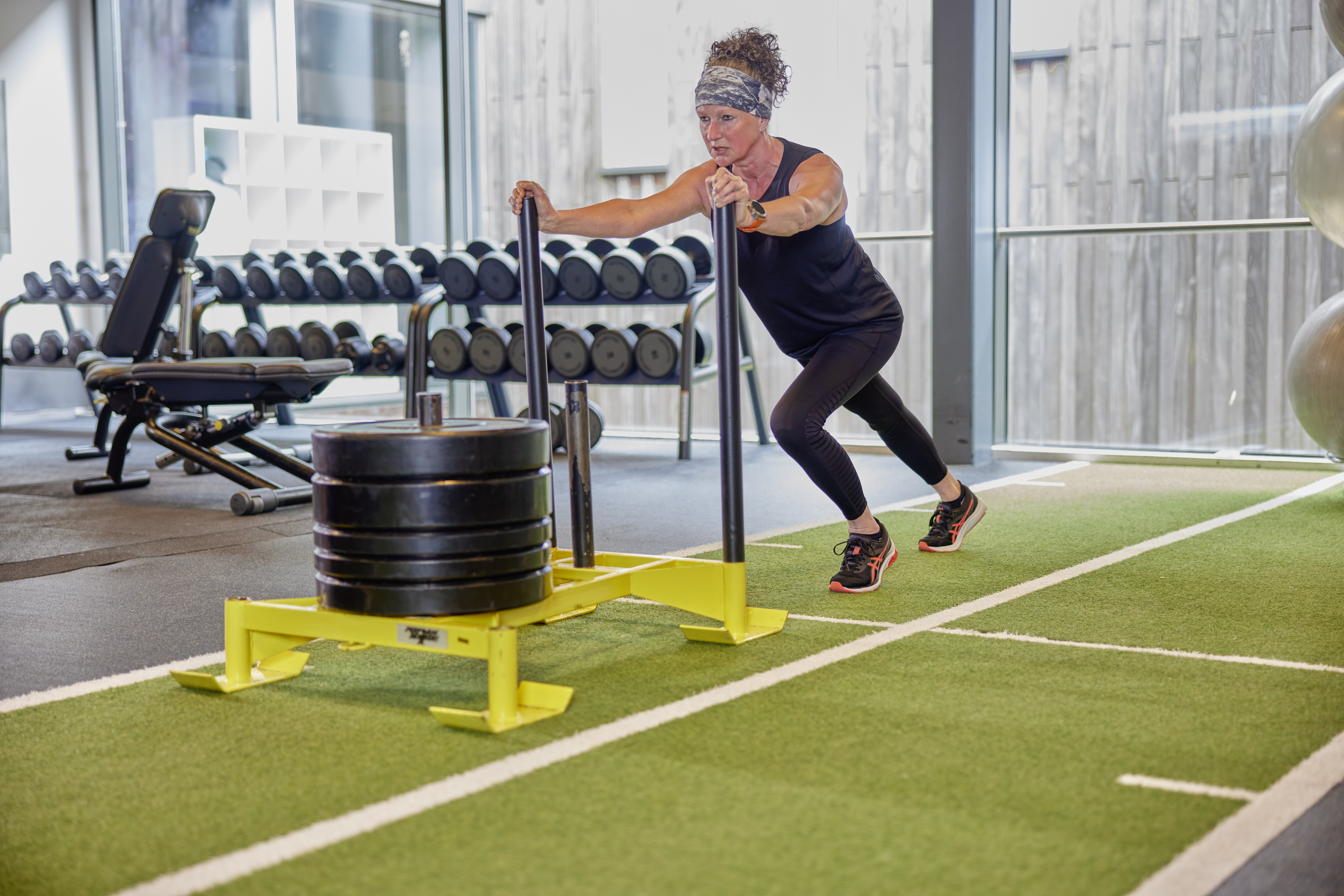 Een vrouw is geconcentreerd aan het trainen in een healthclub van Optisport: ze duwt zware gewichten vooruit en traint hiermee diverse spiergroepen.