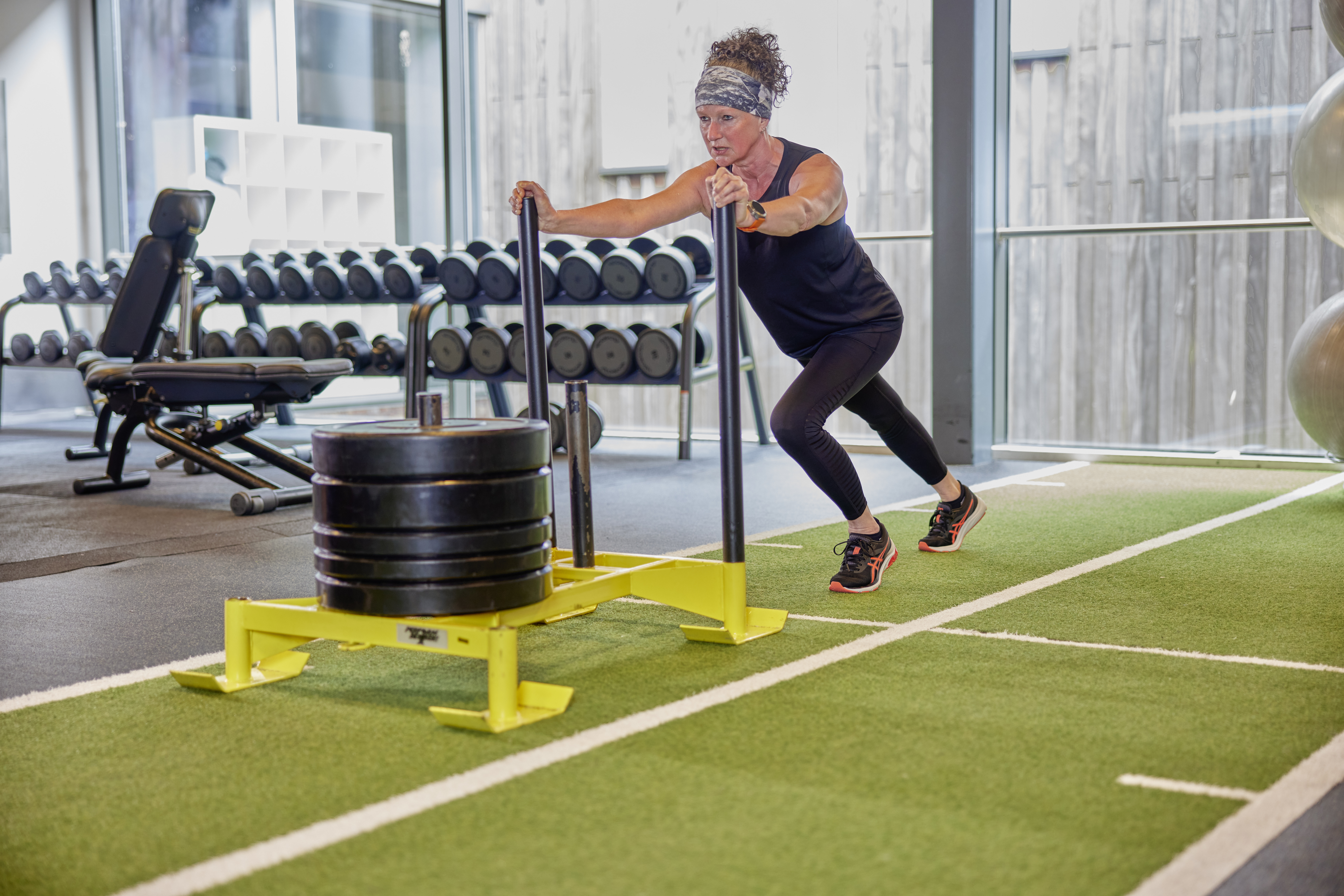 Een vrouw is geconcentreerd aan het trainen in een healthclub van Optisport: ze duwt zware gewichten vooruit en traint hiermee diverse spiergroepen. 