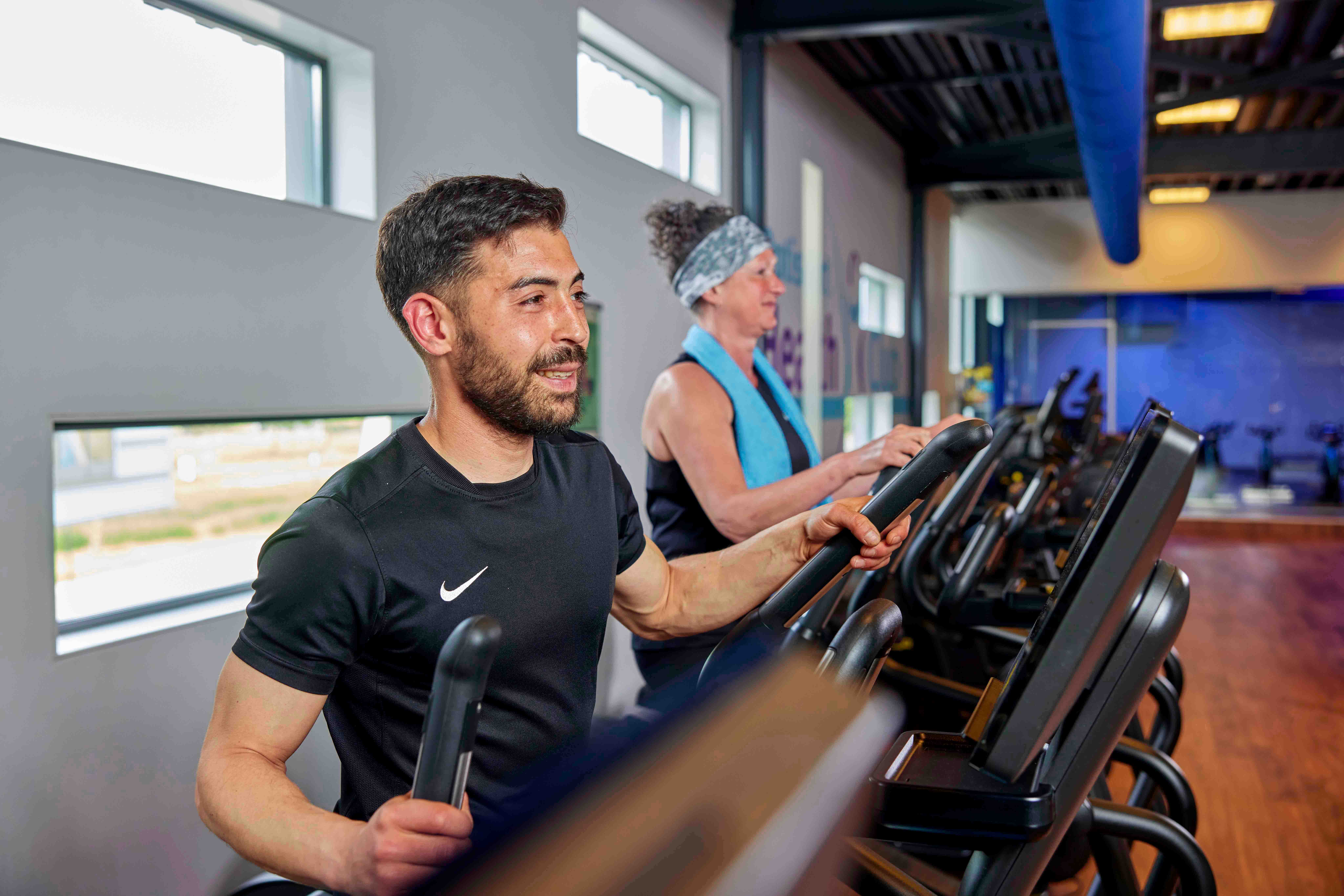Met zichtbaar plezier trainen twee sporters op fitnessapparaten in een healthclub van Optisport. 
