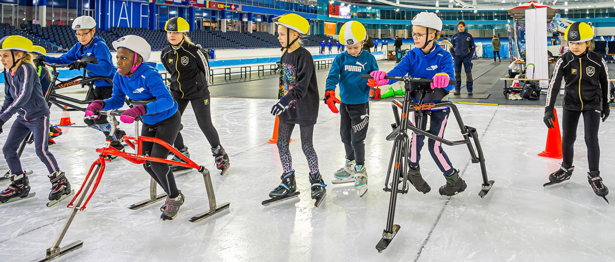 Drie kinderen aan het Frameschaatsen tussen andere kinderen op normale schaatsen