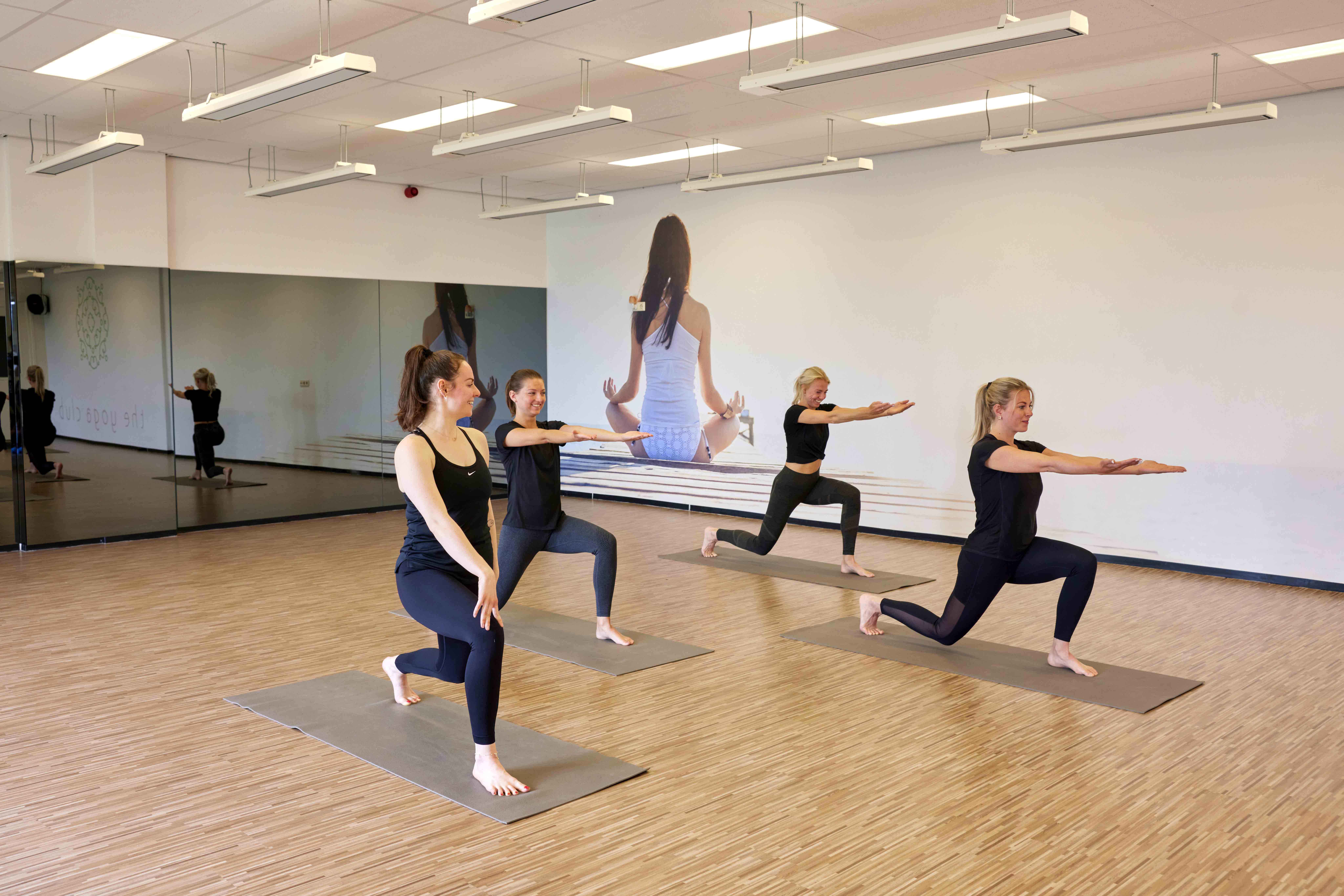 Vier vrouwen sporten samen tijdens een les Pilates bij Optisport, waarbij iedereen op zijn eigen niveau kan meedoen: een weldaad voor lichaam en geest! 