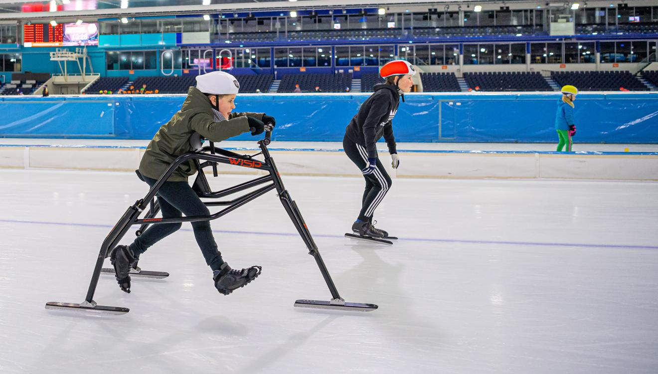 Jongetje aan het Frameschaatsen naast hem een jongen op normale schaatsen