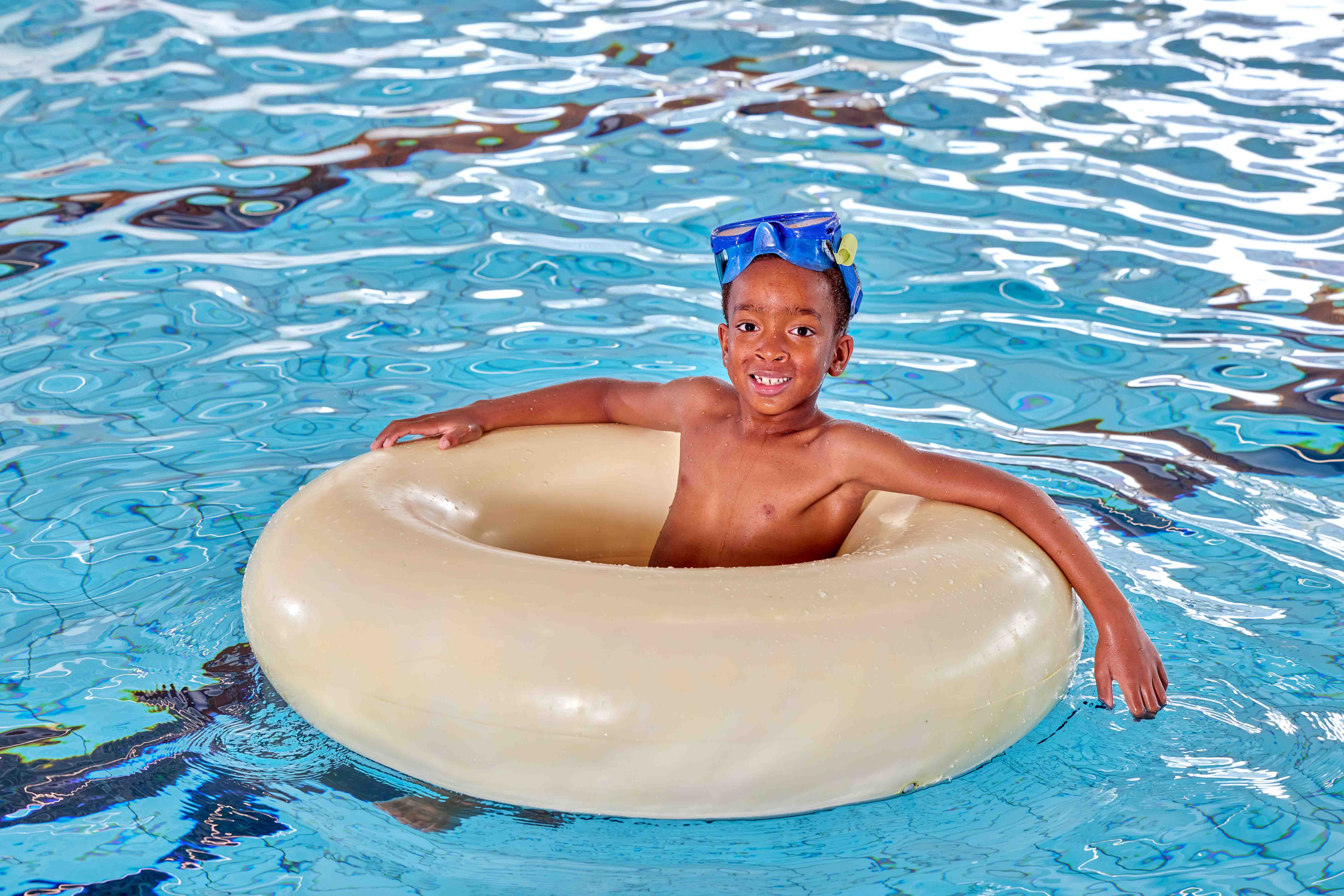 Een jongetje met een grote duikbril op drijft comfortabel in een grote zwemdonut in het zwembad van Optisport, tijdens het Vrijzwemmen. 