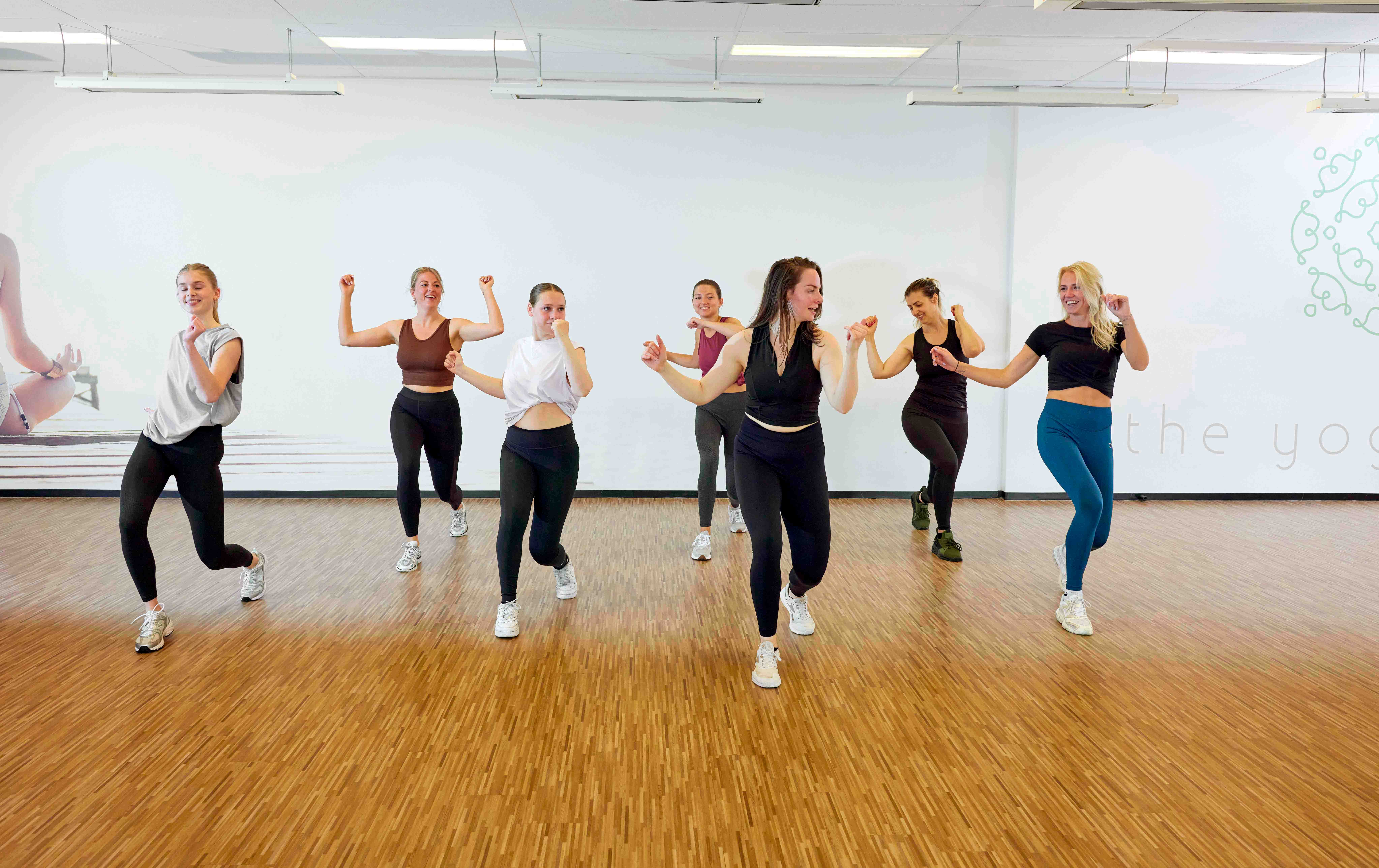 Een groep jonge vrouwen geniet van de les Zumba bij Optisport: een workout waarin fitness en dans samen komt, voor optimale vetverbranding. 