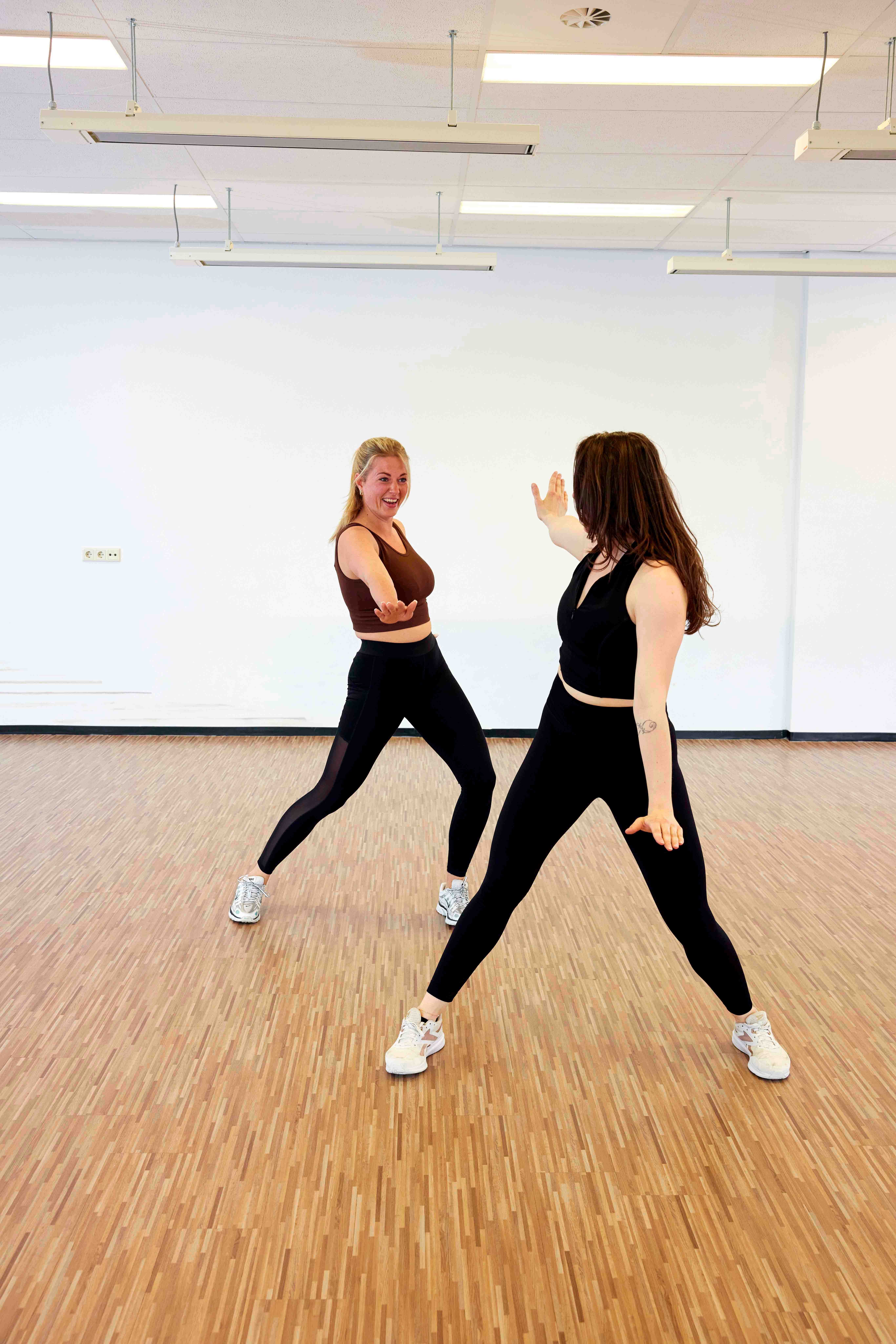 Twee vrouwen oefenen een danspasje tijdens de Zumba groepsles op een van de locaties van Optisport. 