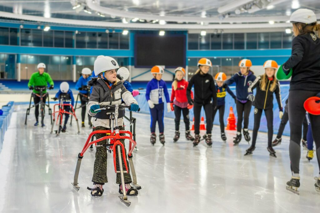 Kindje is aan het Frameschaatsen met daarachter een grote groep kinderen op schaatsen 