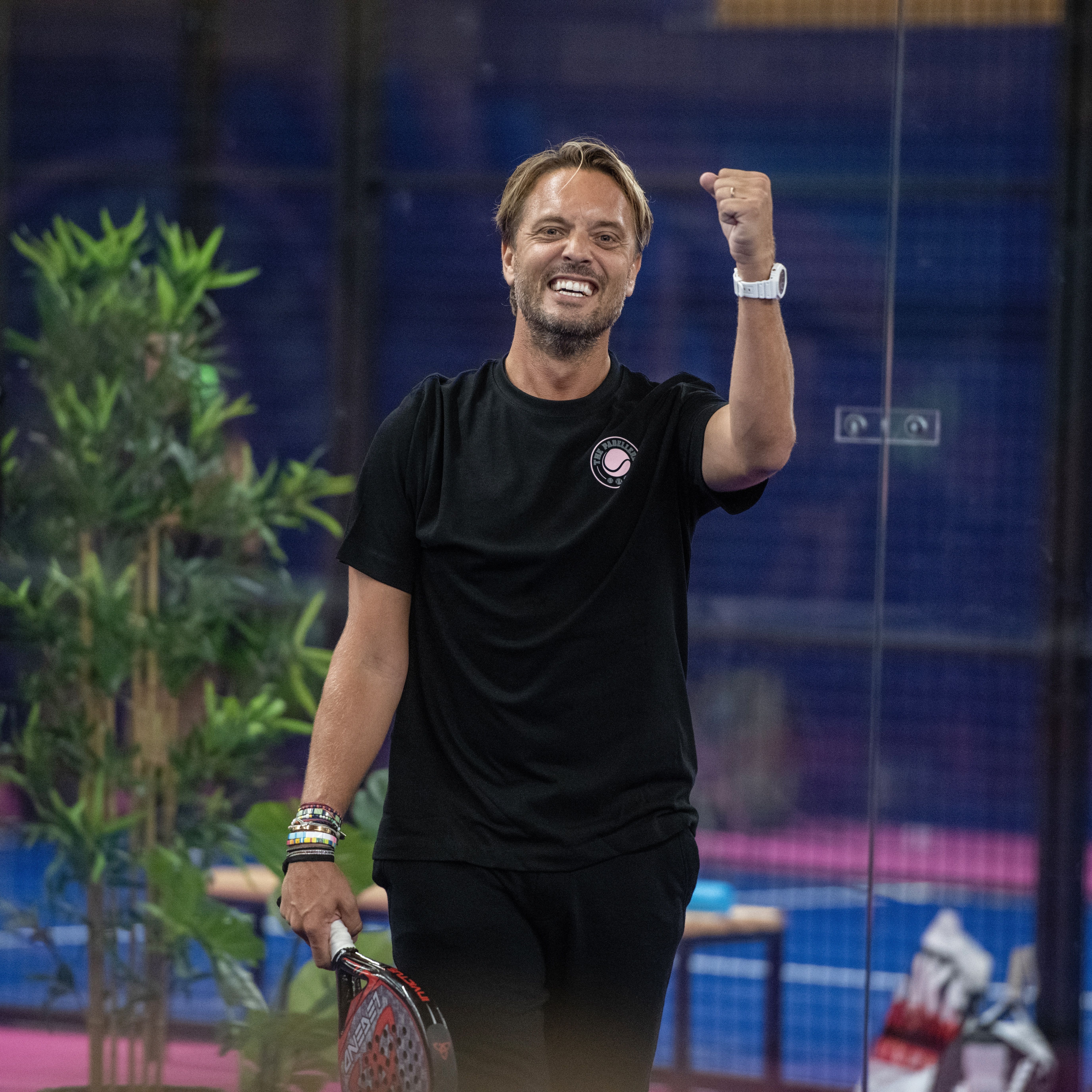 Een man kijkt blij op de padelbaan tijdens het padellen.