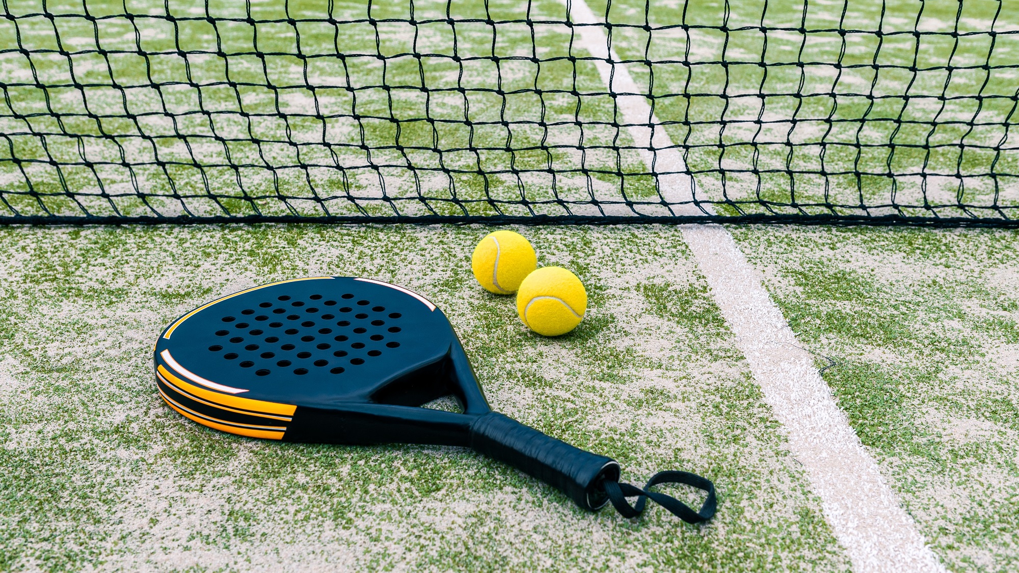 Een padelracket met ballen liggen op de grond.