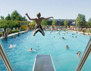 Jongen springt met armen en benen wijd van de duikplank